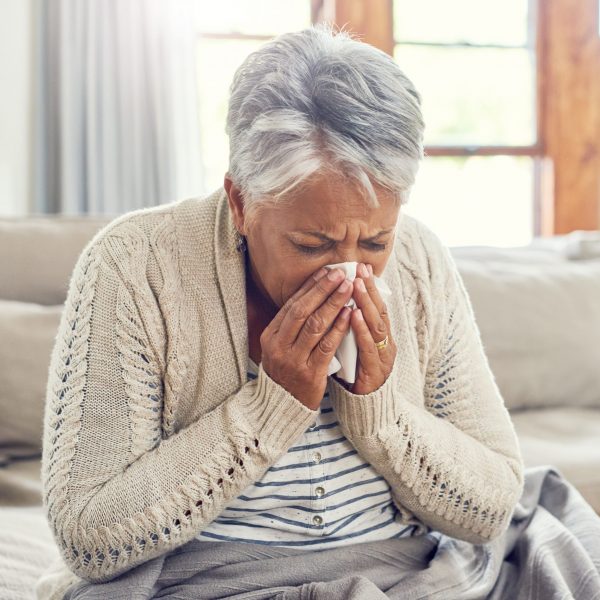 Senior woman, sick and blowing nose at home from virus, allergy and illness on couch. Tired, tissue and elderly female person in a house lounge with sneeze from covid and flu on a sofa with allergies.