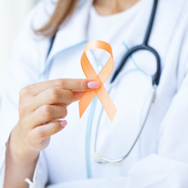 Close up of a doctor holding and showing orange awareness ribbon in her hands.
